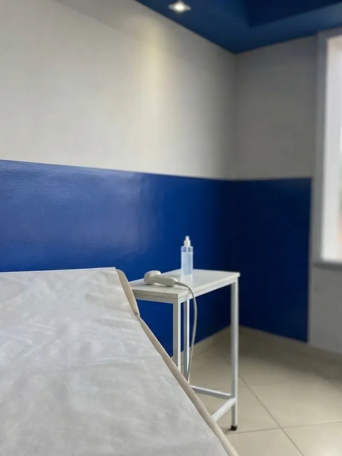 Sala de exame com maca e, na mesa de apoio, o transdutor e o frasco de gel